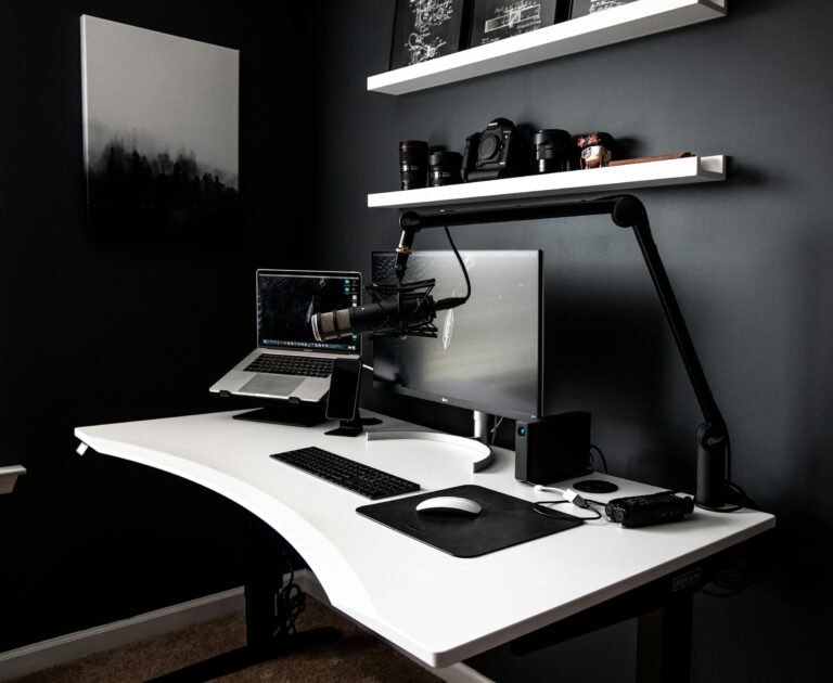 Contemporary style workspace with netbook near computer and microphone on white table in room with dark walls